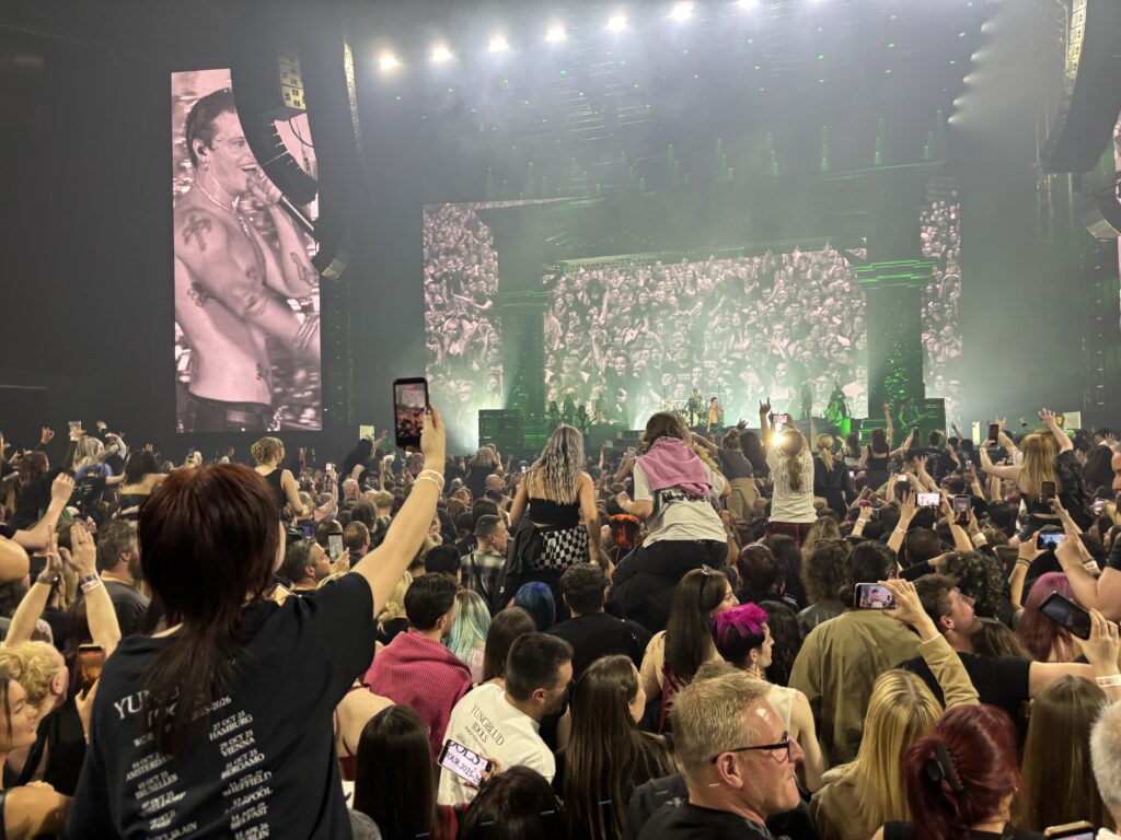 Yungblud, Yungblud live, Idols World Tour, Birmingham Utilita Arena, Birmingham, A view above people's heads with some sat on shoulders and some holding phones with a shirtless man on stage and an image of him on a big screen to the side of the stage