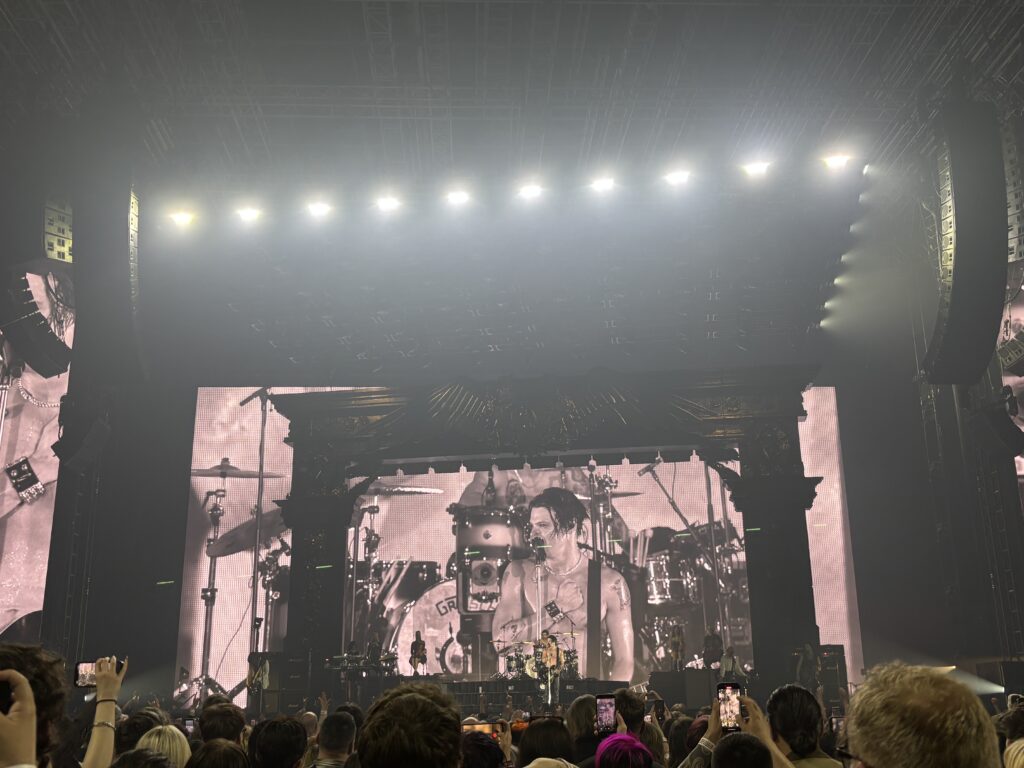 Yungblud, Yungblud live, Idols World Tour, Birmingham Utilita Arena, Birmingham, A crowd in front of a dark stage with a shirtless male singer just visible in front of a large screen showing his image