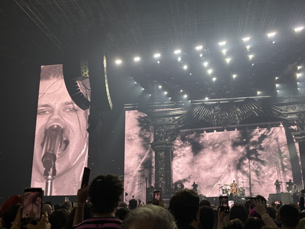 Yungblud, Yungblud live, Idols World Tour, Birmingham Utilita Arena, Birmingham, Silent Sunday, My Sunday Photo, A crowd in a dark arena with a band just visible on stage with a shortless man singing and his face large on a sceen to the side of the stage