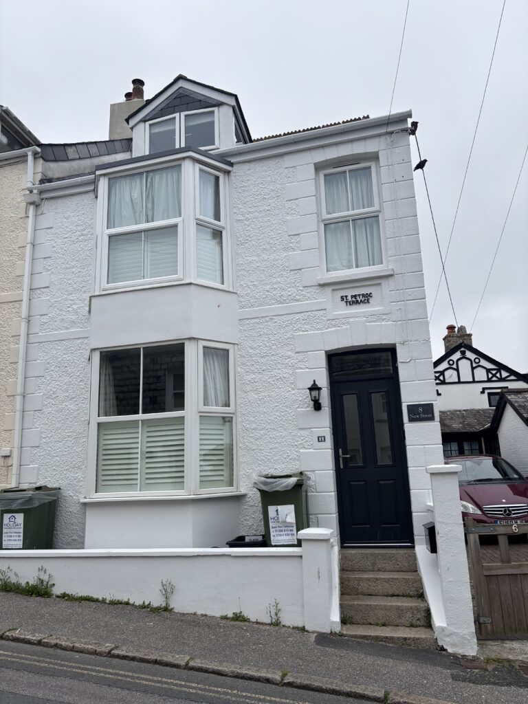 8 New Street, Padstow, Cornwall, Holiday, A three storey white house with steps up to the black front door stands against a grey sky