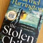 The Stolen Child by Carmel Harrington, The Stolen Child, Carmel Harrington, Book review, A book called The Stolen Child by Carmel Harrington with some steps the sea and a small yellow rucksack on the cover sits on a wooden table
