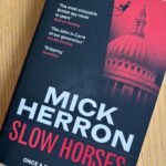 Slow Horses by Mick Herron, Book review, Slow Horses, Mick Herron, A red and black book called Slow Horses by Mick Herron with St Paul's Cathedral on the cover sits on a wooden table