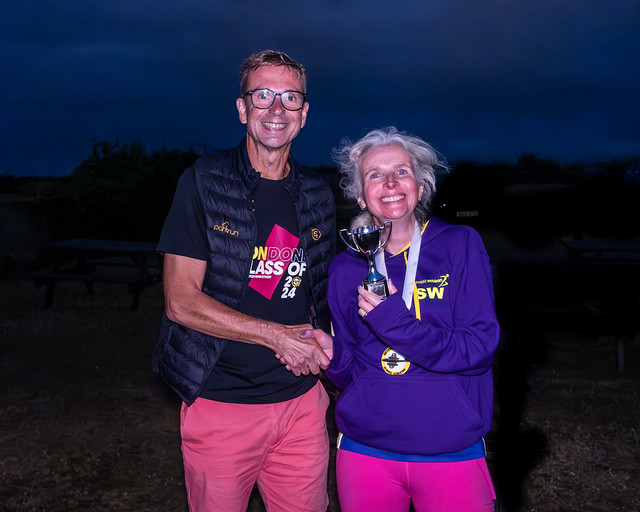 Meteor Mile prize, Meteor Mile, A tall man in glasses shakes hands with a smiling woman in a purple hoodie holding a trophy against the night sky