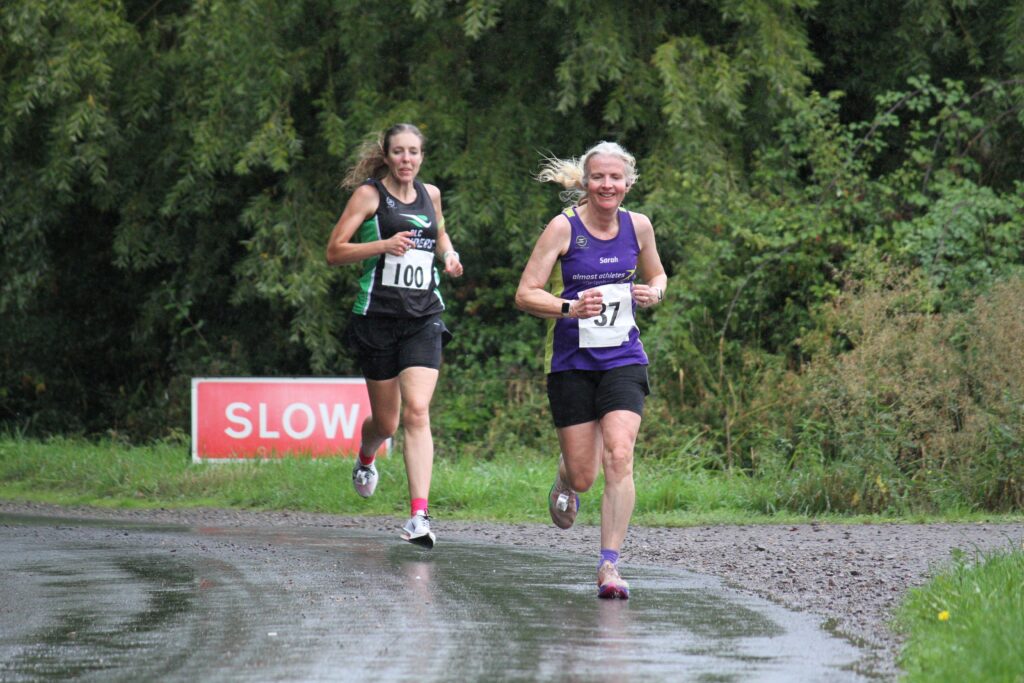 Angels 10k, Running, Runner, Two female runners running along a wet road with trees in the background and a red slow sign