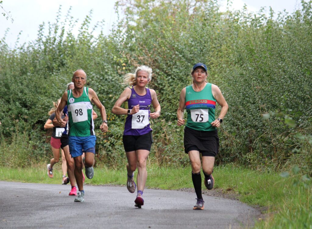 Angels 10k, Running, Runners, Two female and one male runner in vests and shorts running along a country lane with hedges alongside
