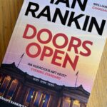 Doors Open by Ian Rankin, Doors Open, Ian Rankin, Book review, A book called Doors Open by Ian Rankin with a grand building at sunset on the cover sits on a wooden table