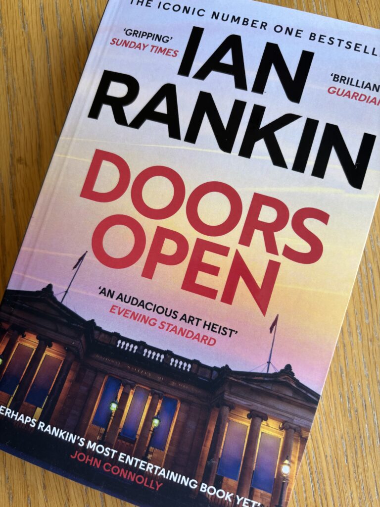 Doors Open by Ian Rankin, Doors Open, Ian Rankin, Book review, A book called Doors Open by Ian Rankin with a grand building at sunset on the cover sits on a wooden table