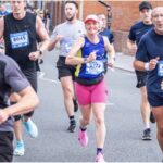 Running, Runner, Cheltenham half marathon, A female runner in a purple vest with pink cap and shorts and trainers runs along a road surrounded by male runners
