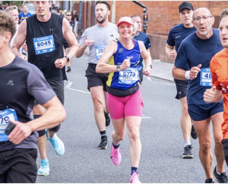Running, Runner, Cheltenham half marathon, A female runner in a purple vest with pink cap and shorts and trainers runs along a road surrounded by male runners