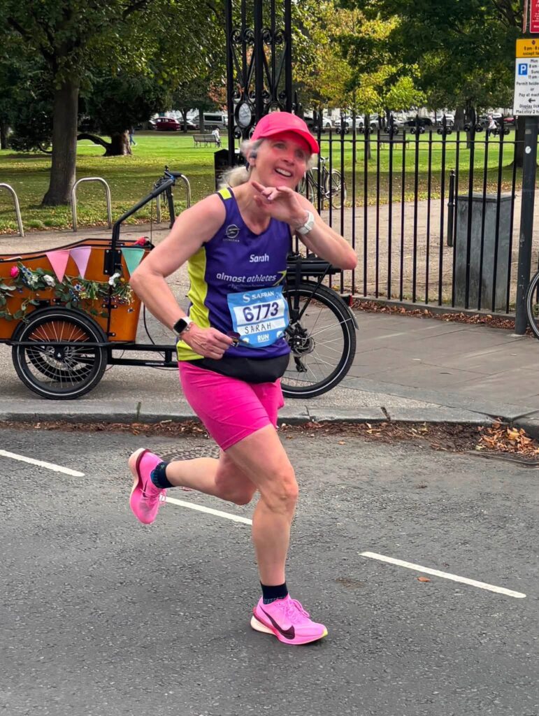 Running, Runner, Cheltenham half marathon, A female runner in a purple vest with pink cap and shorts and trainers runs along a road with a park in the background