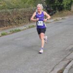 Sharpness 4, Running, Runner, A female runner in a purple vest with a race number runs along a country lane with autumnal hedges in the background