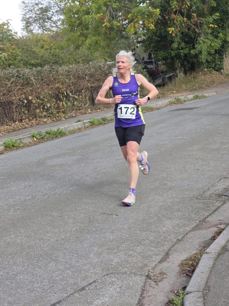 Sharpness 4, Running, Runner, A female runner in a purple vest with a race number runs along a country lane with autumnal hedges in the background