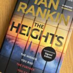 The Heights by Ian Rankin, Book review, The Heights, Ian Rankin, A colourful book called The Heights by Ian Rankin with the silhouette of a landscape including The Shard on the cover sits on a wooden table