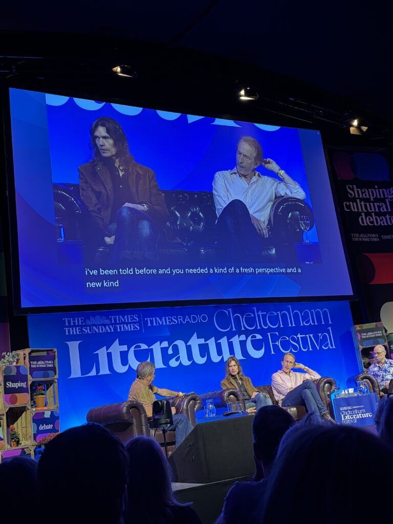 Suede at Cheltenham Literature Festival, Silent Sunday, My Sunday Photo, Four middle aged men sit in front of a blue background which says Cheltenham Literature Festival and two of them are visible on a large screen above their heads